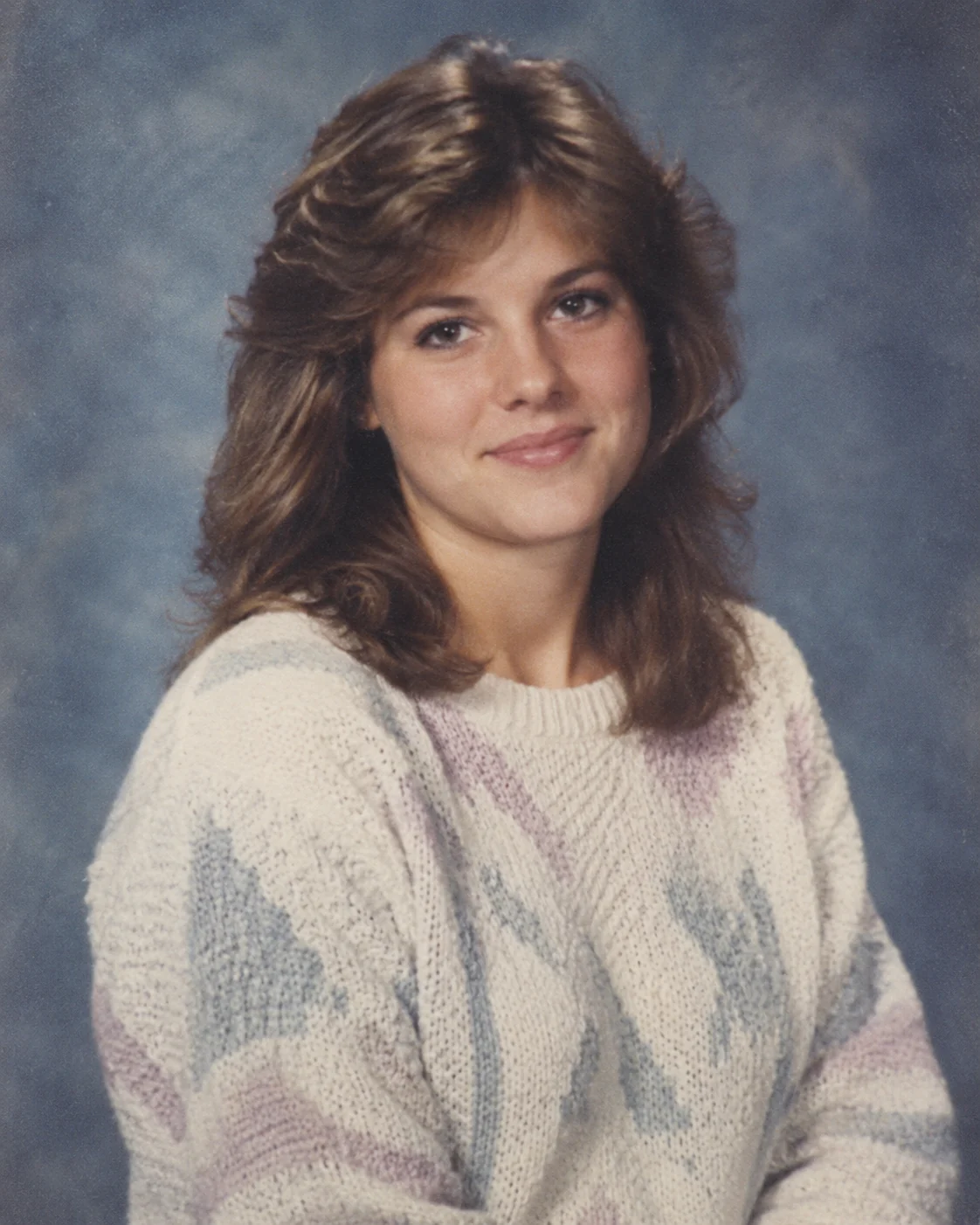 Original AI-generated example of a fictional adult 1986 yearbook portrait against a muted blue-gray backdrop.